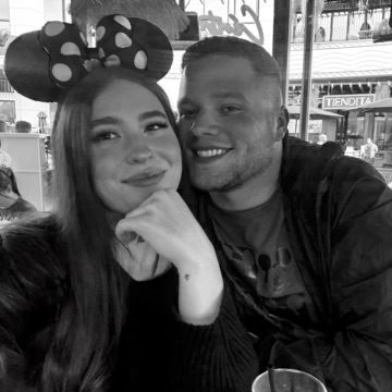 Jaden in Minnie Mouse ears smiling next to her partner at an outdoor table